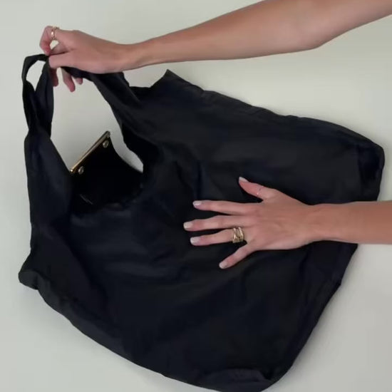 Hands holding the unfolded black Olniy tote, with the pouch still attached