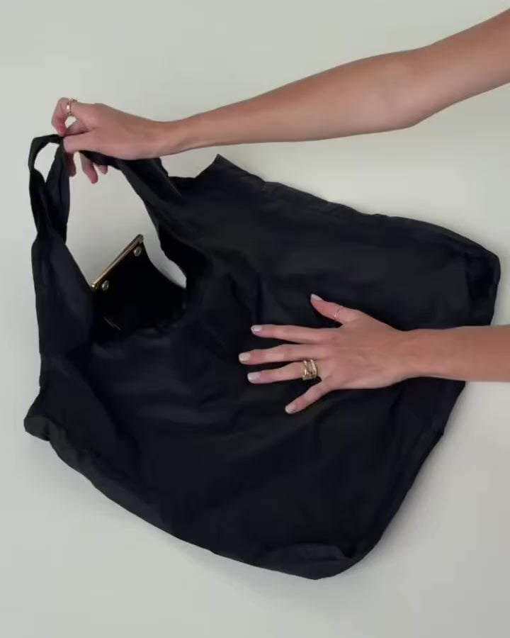 Hands holding the unfolded black Olniy tote, with the pouch still attached